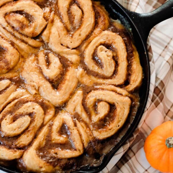 sourdough pumpkin cinnamon rolls in a cast iron skillet on a brown plaid napkin with two small pumpkins to the right