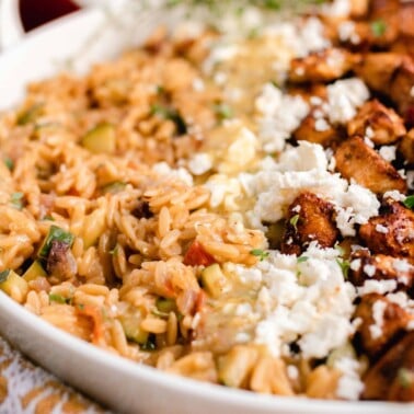 side view of a white dish with Greek orzo pasta with layers of feta cheese and marinated chicken