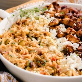 side view of a white dish with Greek orzo with layers of feta, chicken, and olives.