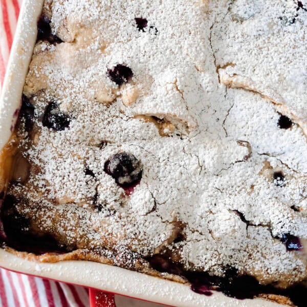 overhead photo of a baking dish with marscapone stuffed sourdough French toast casserole dusted with blueberries and dusted with powdered sugar in a red and white baking dish.