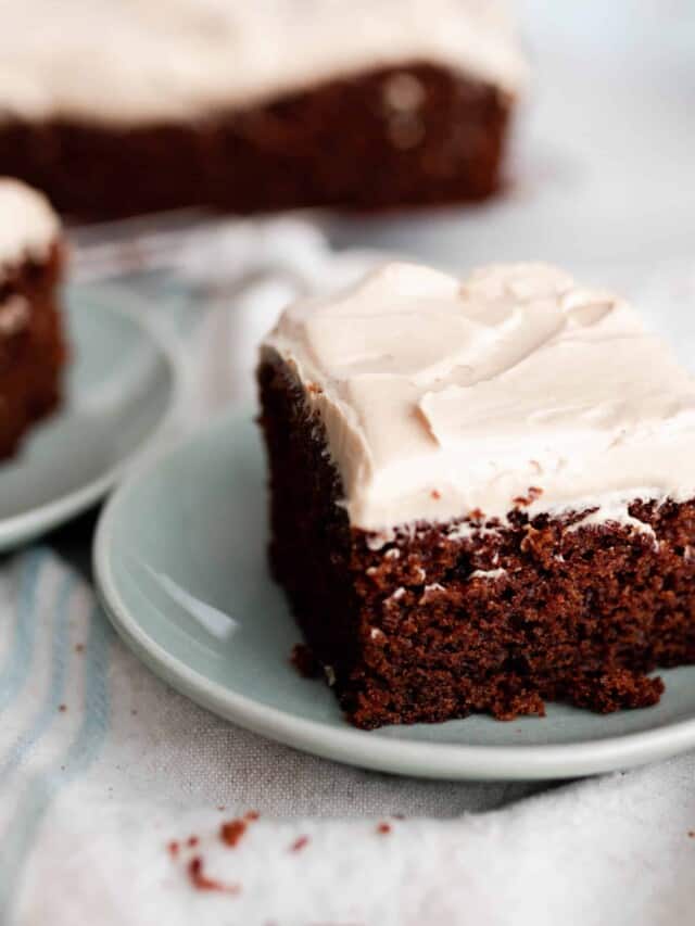 square slices of einkorn gingerbread cake topped with mocha frosting on light teal plates on a white countertop