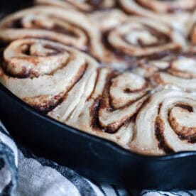 sourdough cinnamon buns fresh out of the oven in a cast iron skillet on top of a white and black stripped towel