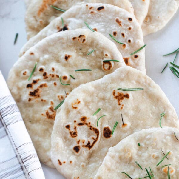 sourdough flat bread topped with fresh rosemary layered in a line on a white quartz countertop with a plaid towel to the left