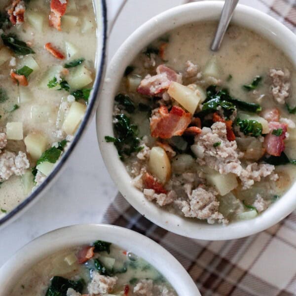 two bowls of cuppa toscana soup with potatoes, sausage, bacon, kale in white bowls with a pot of soup to the left.