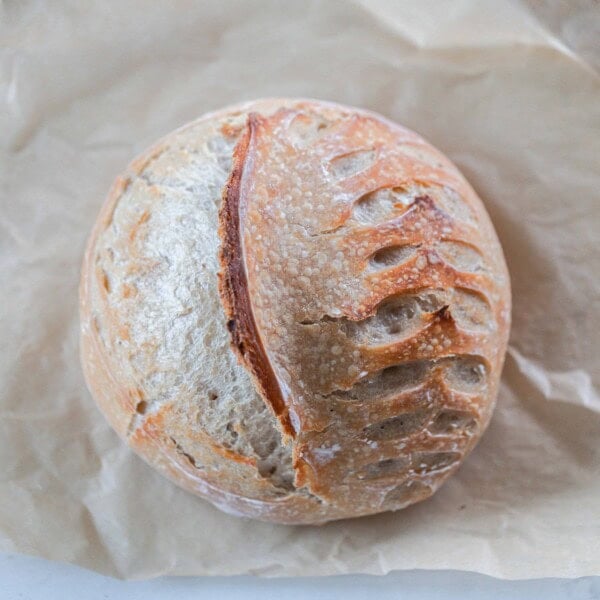 overhead photo of a loaf of sourdough bread with a wheat and half moon shaped pattern in it on parchment paper