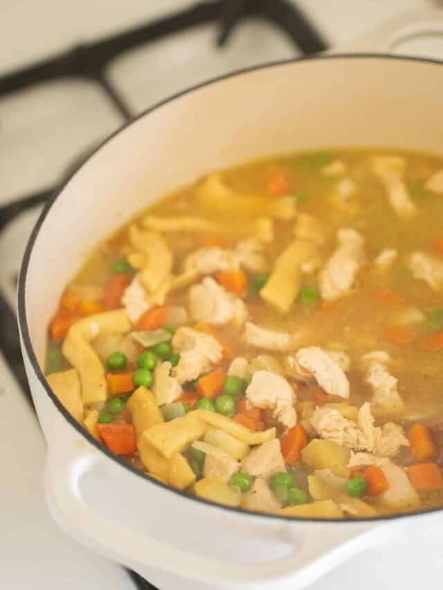 chicken noodle soup with homemade noodles in a white dutch oven on a white stove