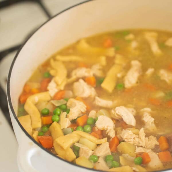 chicken noodle soup with homemade noodles in a white dutch oven on a white stove