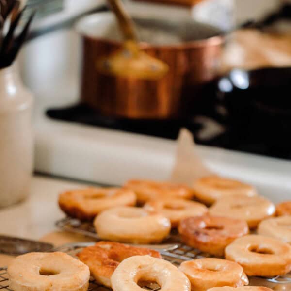 glazed sourdough donuts stacked on a wire rack next to a white vintage stove with a copper pot on the stove