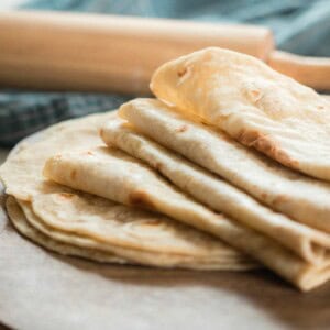 sourdough tortillas folded in half on a white quarts countertop with a blue towel with a rolling pin resting on top in the background