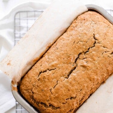 overhead photo of sourdough zucchini bread in a parchment lined stainless steel loaf pan on a wire rack over a white towel