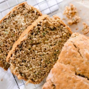 a loaf of sourdough zucchini bread with two slices layer out in from to the loaf on a wire rack