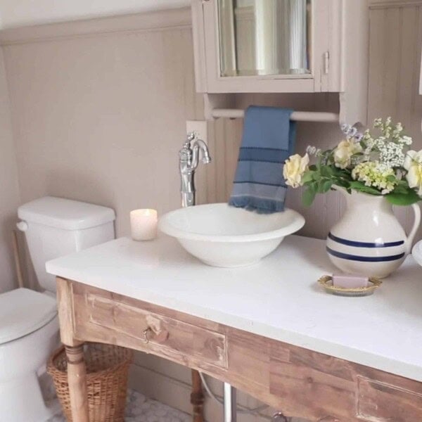 farmhouse kids bathroom with a custom antique inspired vanity with a marble top and antique bowl vessel sinks. Two medicine cabinets hang above the sinks with blue towels hanging off the cabinets