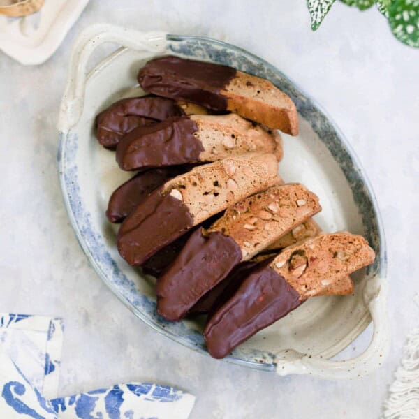 sourdough biscotti dipped in chocolate on a white and blue vintage platter on a gray countertop with a blue floral towel in the right corner