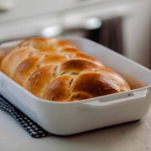 sourdough challah fresh out of the opven in a white baking dish on a pot holder on a white countertop