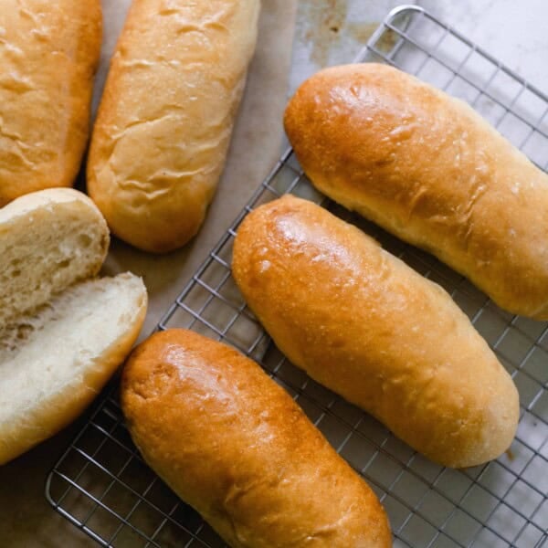 6 sourdough hot dog buns on a wire rack with one sliced open