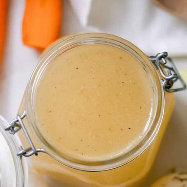 overhead photo of a chicken broth in a swing top jar with celery, garlic, carrots and a wooden spoon surrounding the jar