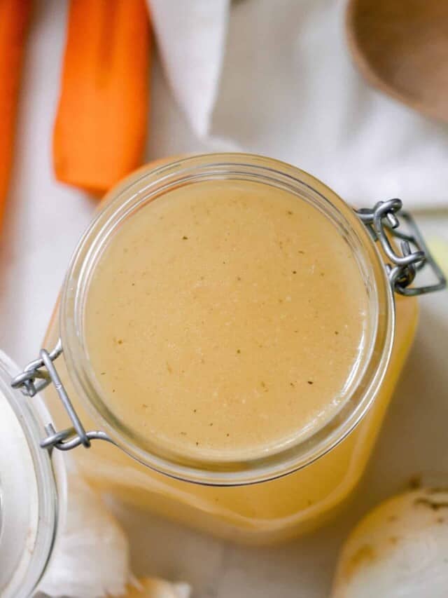 overhead photo of a chicken broth in a swing top jar with celery, garlic, carrots and a wooden spoon surrounding the jar