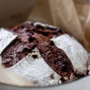 side view of a loaf of chocolate sourdough bread in a parchment lined dutch oven