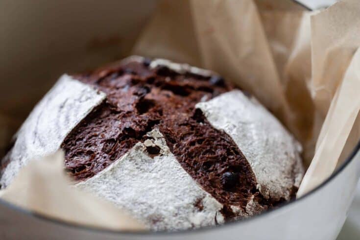 side view of a loaf of chocolate sourdough bread in a parchment lined dutch oven