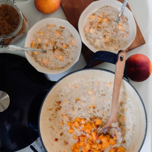 a dutch oven and two bowls full of peaches and cream oatmeal on a vintage stove