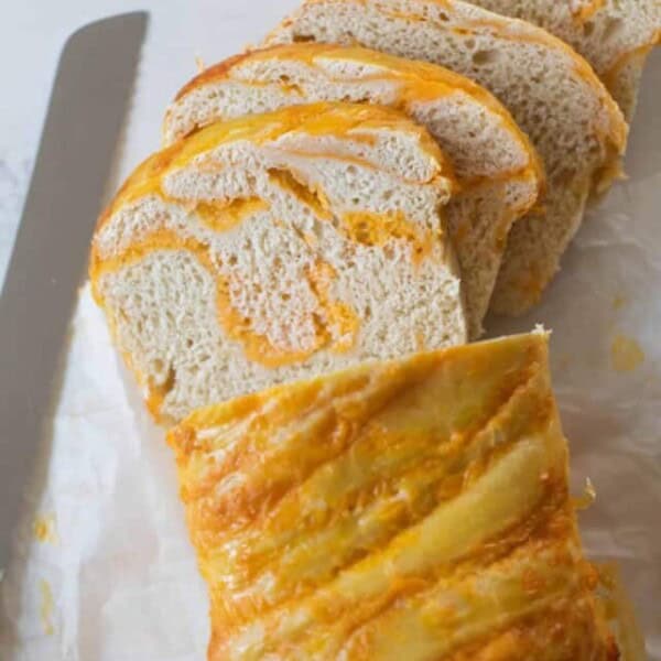 loaf of sourdough cheese bread sliced up on parchment paper with a bread knife to the left