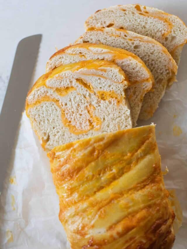 loaf of sourdough cheese bread sliced up on parchment paper with a bread knife to the left