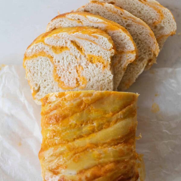 a loaf of sourdough cheese bread with half the loaf sliced into pieces on parchment paper on a white countertop