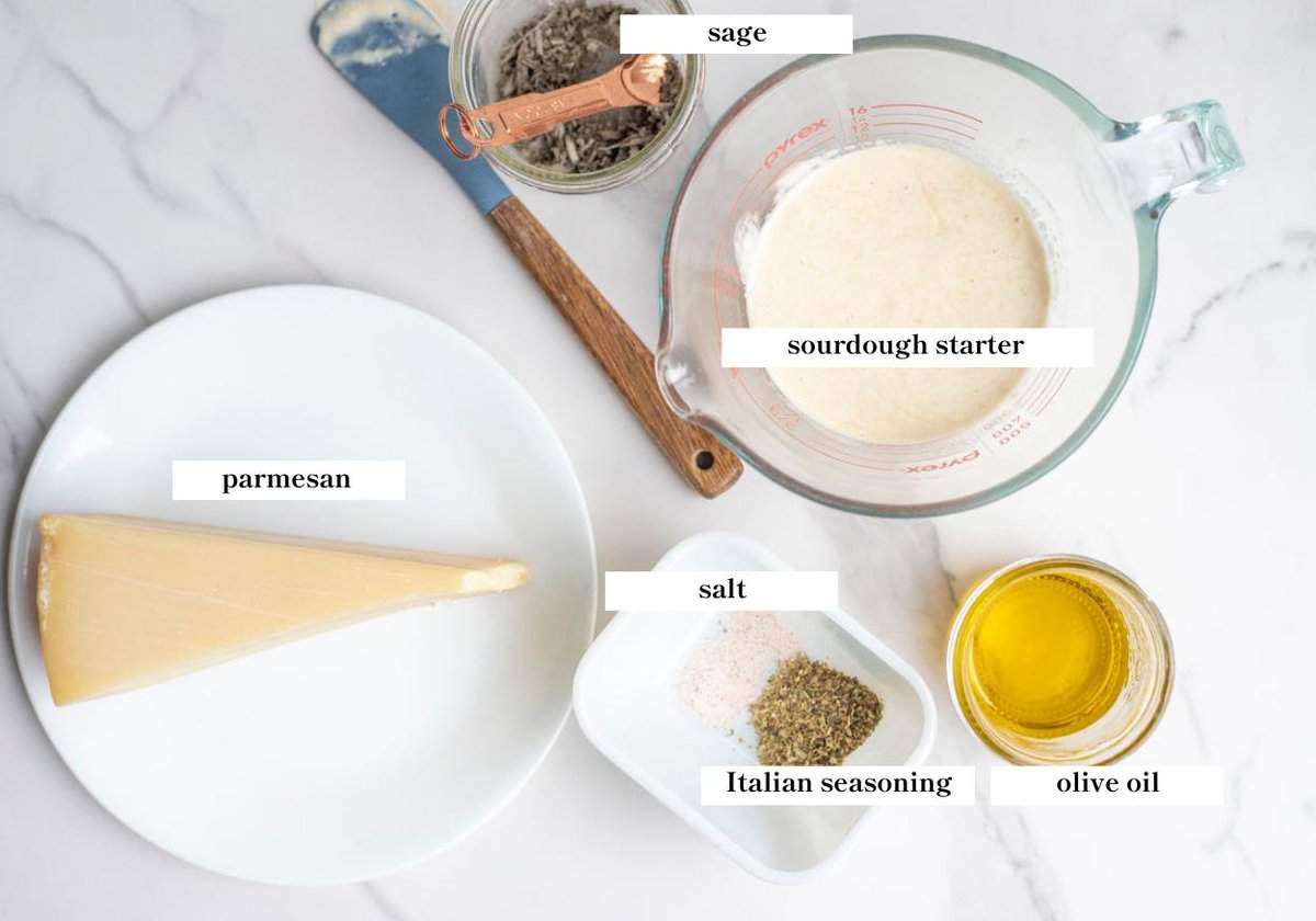 Sourdough starter, olive oil, seasonings, salt, and a block of Parmesan cheese on a marble countertop. 