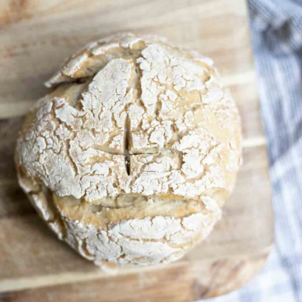 overhead photo of sourdough gluten free bread on a wooden cutting board on top of a white and blue stripped towel