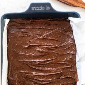 overhead photo of sourdough brownie batter poured into a blue 9x0 baking dish with a wooden spatula in the back right corner