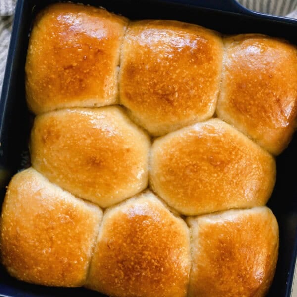 overhead photo of sourdough dinner rolls with a deep golden shiny top in a dark navy baking dish