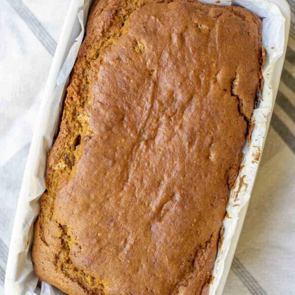 overhead photo of sourdough pumpkin bread in a cream stone loaf pan on a white and blue stripped towel