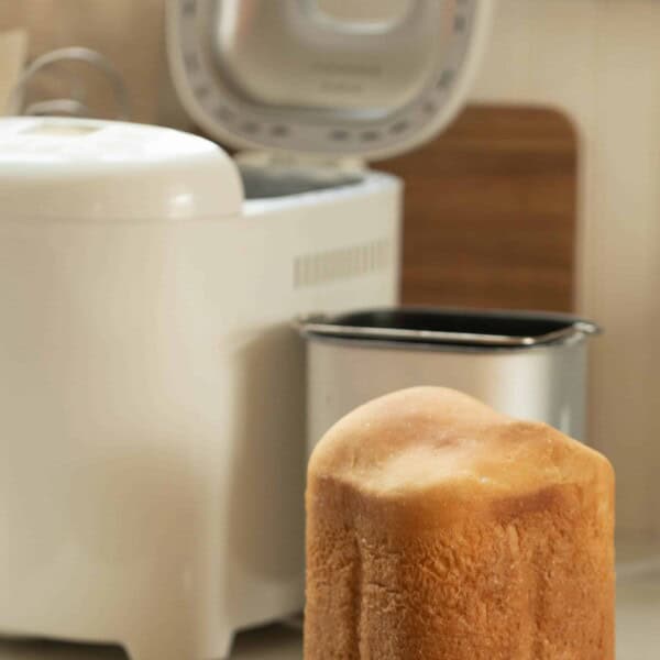 sourdough bread right out of the bread machine on a white countertop with the bread machine and baking pan in the background