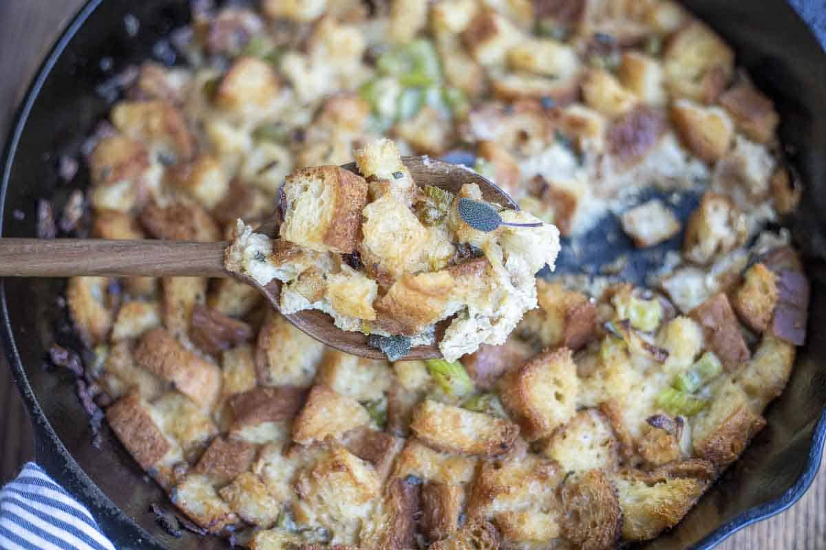 Gluten free stuffing in a cast iron skillet with a spoon of stuffing held in front of the skillet.