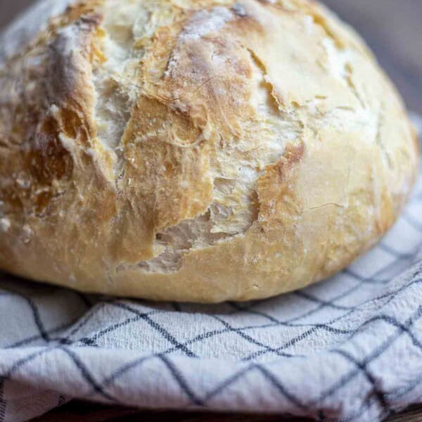 loaf of crusty sourdough discard bread on a white and black checked towel on a wood table