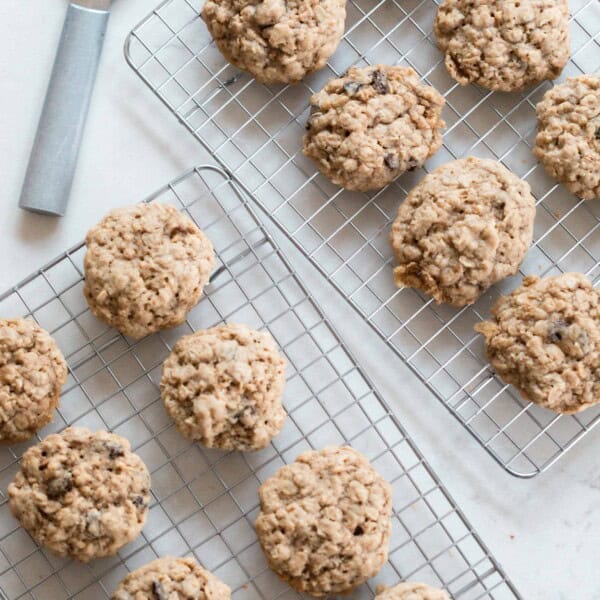 overhead photo of two wire racks full of oatmeal cookies on a white countertop with a metal spatula in the back corner