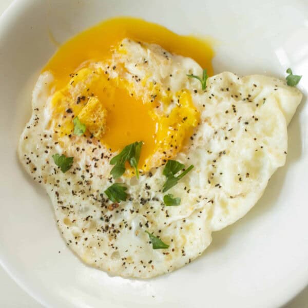 overhead photo of over easy eggs topped with fresh herbs on a white plate