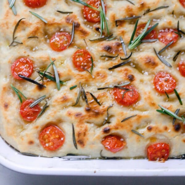 overhead photo of 1/4 of a white baking dish with sourdough focaccia topped with tomatoes and fresh rosemary