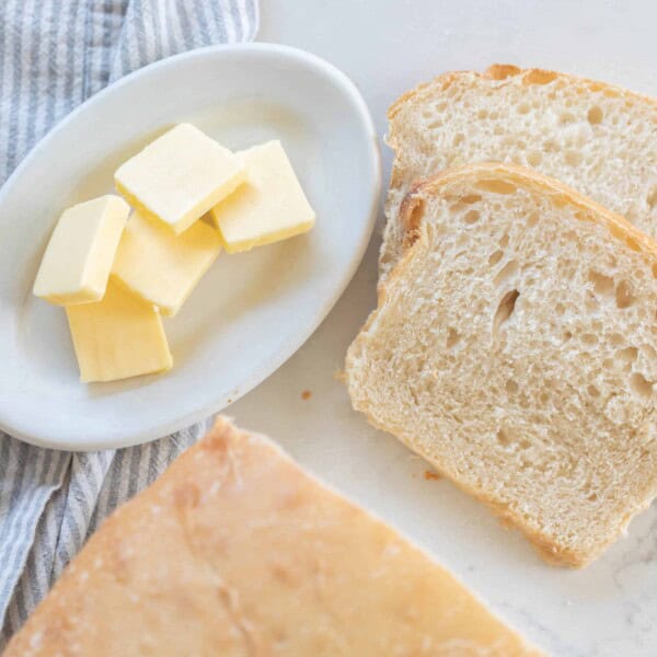 sourdough potato bread sliced on a white countertop with a plate of butter to the left