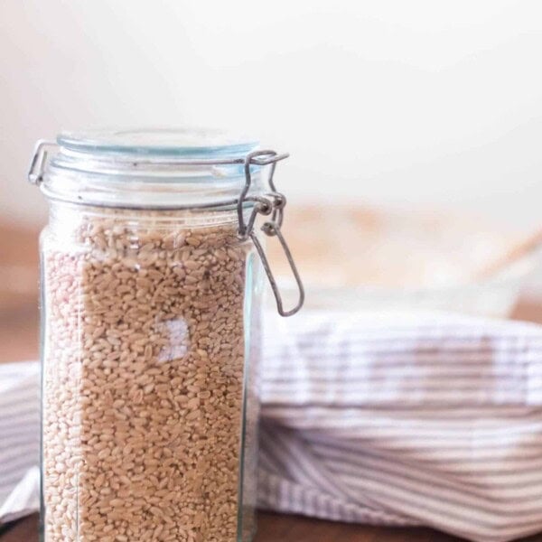 swing top jar full of wheat berries on a wood table with a blue and white towel behind it.