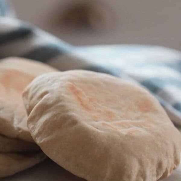 four sourdough pita breads on a white countertop with a white and blue stripped towel and bowl in the background