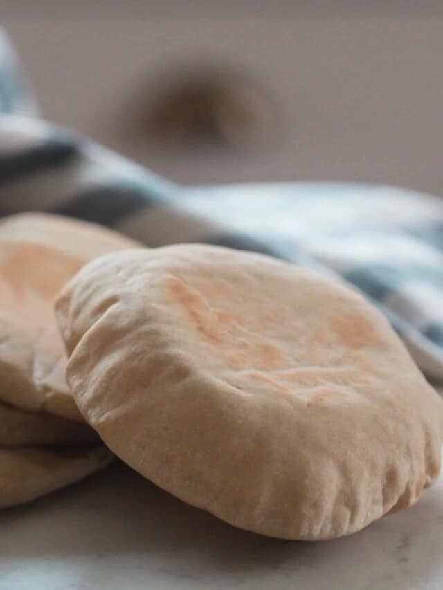 four sourdough pita breads on a white countertop with a white and blue stripped towel and bowl in the background