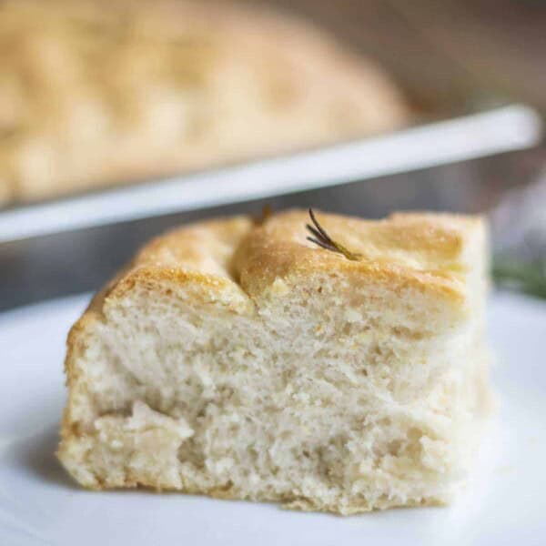 sourdough discard focaccia on a white plate with a tray of more focaccia in the background