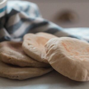 four sourdough pita breads on a white countertop with a white and blue stripped towel and bowl in the background