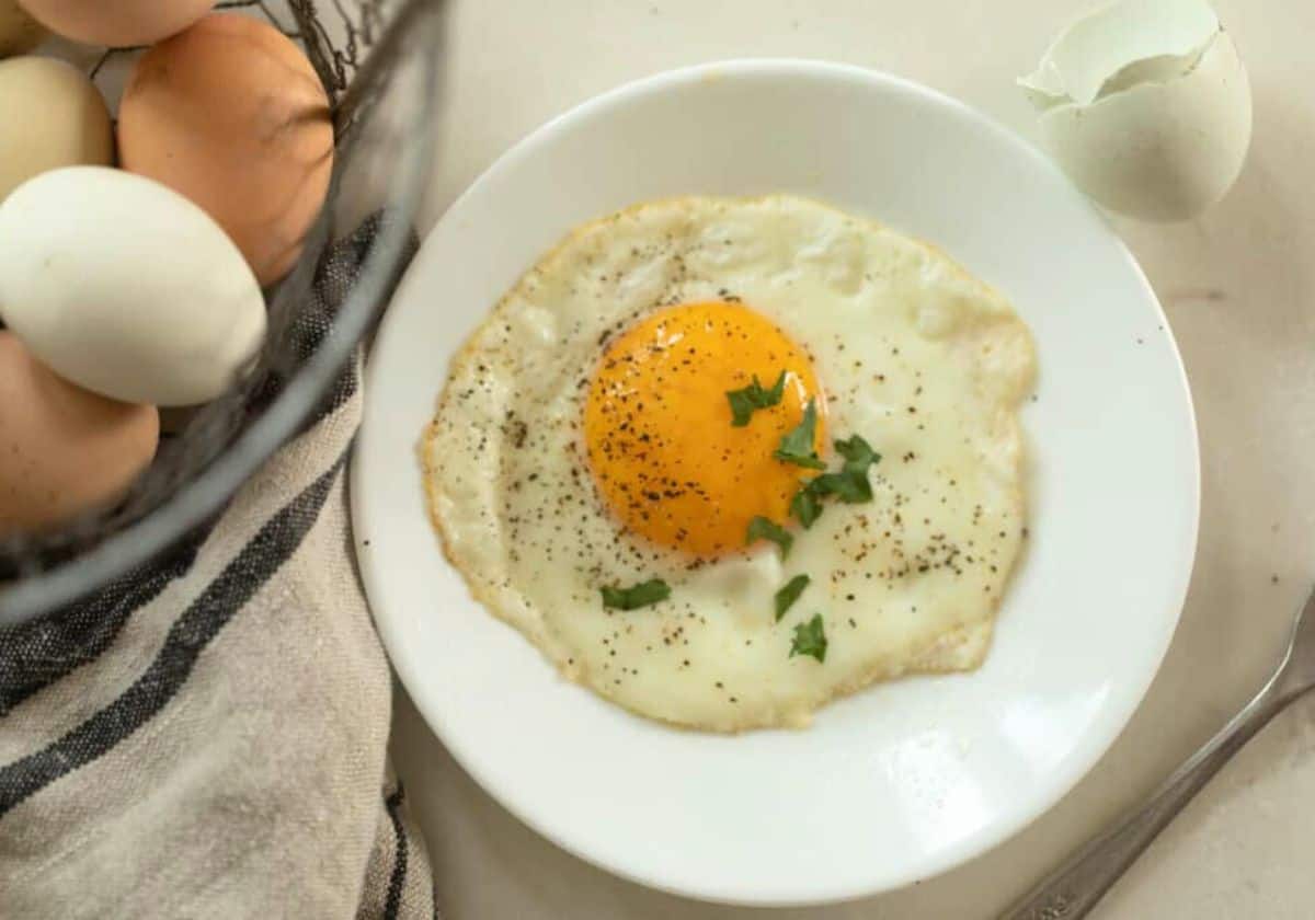 Cooked egg on a plate with a basket of eggs on the side.