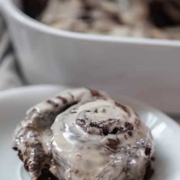 double chocolate sourdough roll with vanilla icing on a white plate with a white baking dish in the background with more rolls