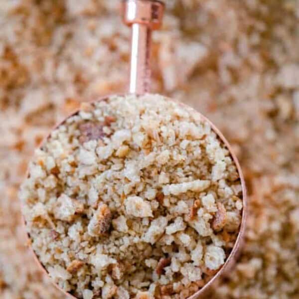 a copper and wood dry measuring cup full of sourdough bread crumbs on a sheet of more breadcrumbs