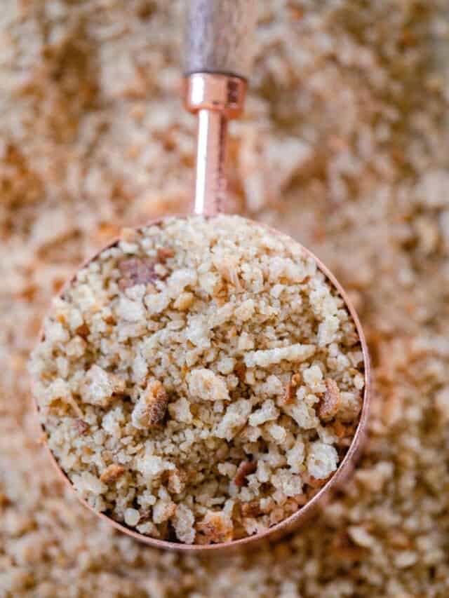 a copper and wood dry measuring cup full of sourdough bread crumbs on a sheet of more breadcrumbs