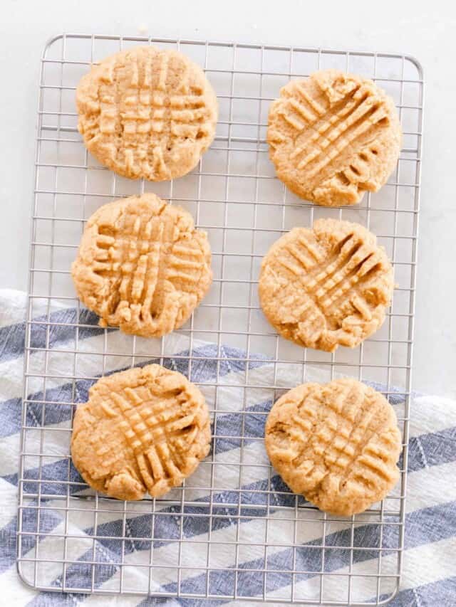 six sourdough peanut butter cookies on a wire rack on a white countertop with a blue and white tea towel