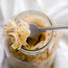 A fork scooping sauerkraut out of a mason jar.